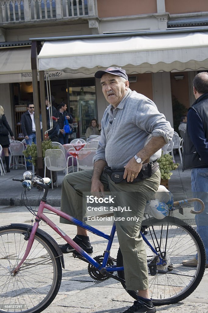 Senior resting on his bicycle in Piazza "Lake Cuomo, Italy - May 1, 2008: Senior resting on his pink and blue bicycle in Piazza in Italy; he's clutching his money pack and thinking about what to do next on a beautiful spring day." Active Lifestyle Stock Photo