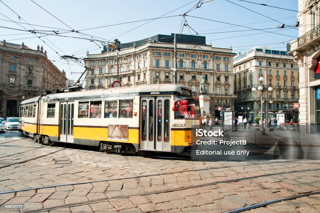 Tram passes through Piazza Cordusio in Milan Milan, Italy - October 2, 2011: Tram passes through Piazza Cordusio with traffic following, building behind is the old stock exchange and statue of the great literary figure Mr. Parini. Also in the background are local people and tourists.   Building Exterior Stock Photo