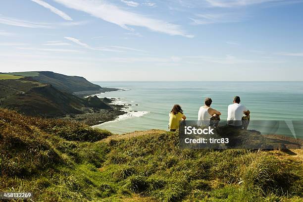 Three Young Adults On Sunlit Cornish Headland Stock Photo - Download Image Now - Beach, Sitting, Three People