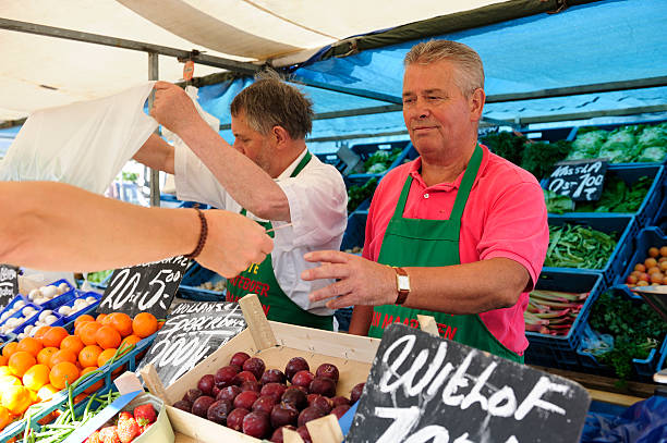 Two greengrocers at an outdoors Dutch market stall "Maarssen, the Netherlands - July 16, 2009: Two greengrocers at work at an outdoors market stall in the town of Maarssen, a few kilometers north of the city of Utrecht. A customer is giving money to the greengrocer." netherlands currency stock pictures, royalty-free photos & images