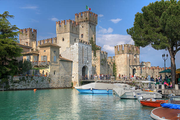 People taking picture at the bright Christmas tree in the Sirmione, one of the beautiful town on the shore of Lake Garda. In background stands out the imposing thirteenth-century castle, the Rocca Scaligera, the historic landmark of the town.