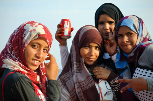 Dahab, Egypt - November 16, 2010: Four Bedouin girls, one holding a Coke with henna-stained fingers, stand outdoors by the sea in this Sinai town situated on the Gulf of Aqaba. Bedouin children, particularly girls, hang around the beachside cafes and approach tourist to try to sell bracelets and other souvenirs.
