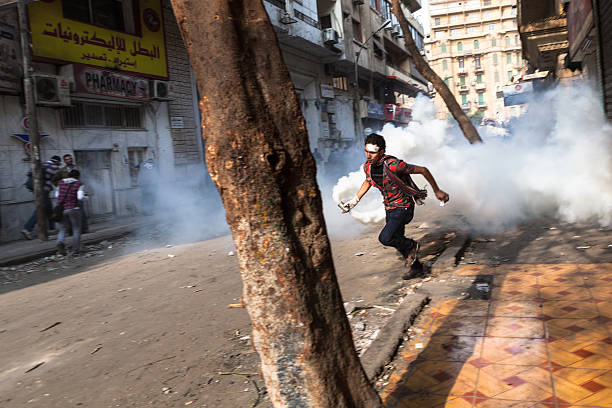 Youth fight back by stealing tear gas canisters in Tahrir "Cairo, Egypt - November 23, 2011: A young man near Tahrir Square is running with a container of riot gas that the police just fired at the protestors." riot tear gas stock pictures, royalty-free photos & images