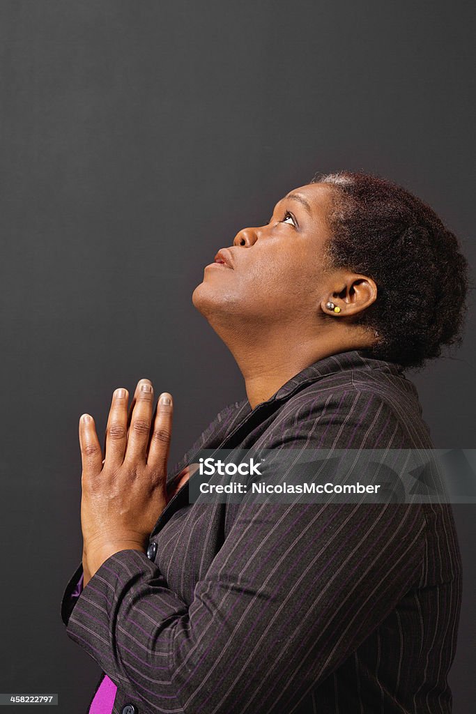 Mature black woman in suit praying looking up Mature black woman in suit praying looking up. Shot against a dark gray background. African-American Ethnicity Stock Photo