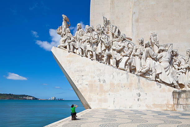 Lisbon, Portugal - July 11, 2012: Monument of the Discoveries in Lisbon, Portugal was inaugurated in 1960 by the Salazar Government. It is situated close to BAlem and overlooking the Tagus River. With an elevator inside the building you can reach a visitors platform on top of the building with a fantastic view over Belem and the Tagus River. A young woman with a green shirt is watching the monument.