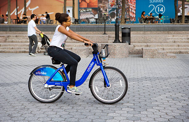 New York City, USA - July 26, 2013: Citi Bike female cyclist rides bicycle at the World Financial Centers Plaza in lower Manhattan, New York City, USA. Citi Bike is New York City's bike sharing system. Intended to provide New Yorkers and visitors with an additional transportation option for getting around the city. There is a credit card charge for the use of the bicycle.