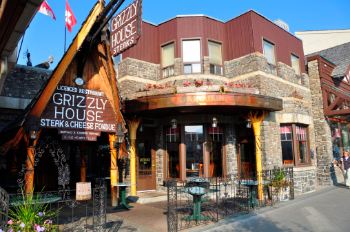 Banff, Canada - September 24, 2012: Grizzly House Steak and Cheese Fondue restaurant on Banff Avenue in Banff National Park, Alberta, Canada. Grizzly House Steak and Cheese Fondue restaurant is a famous Banff landmark and restaurant. Pedestrian visible at right.