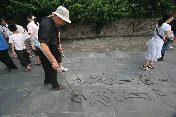 Chinese calligraphy Beijing, China - August 18, 2006: a chinese man writes on the stone floor of the park of Summer Residence of the Emperor. Calligraphy is an old and important art in China and many people in the parks of Beijing like practise themselves with a brush dipped in water. This man is able to write at the same time with both the hands. ambidextrous stock pictures, royalty-free photos & images