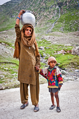 Leh, Jammu and Kashmir, India - July 15th, 2011:Mother in shalwar kameez, with child, carrying water on her head, on the road between Lamayuru and Leh; Northern India.