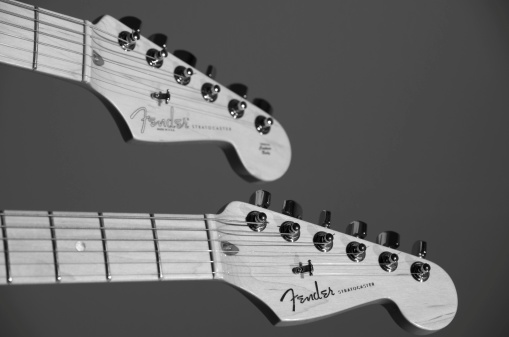 Vancouver, BC, Canada - August 31, 2012: Two maple Fender Stratocasters with focus on the nearer Guitar headstock. Photographed in black and white on a gray background.