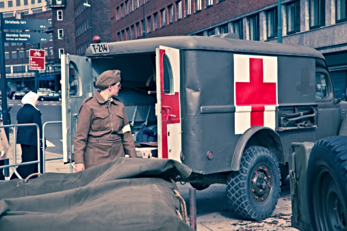Oslo, Norway - September 2, 2012:Lady in uniform at an ambulance and equipment from WW2.  Norway celebrating 100-years of air power. Held  in central Oslo in  front of the  city hall  with many performances of situations from different time periods and situations of war. Cross processed