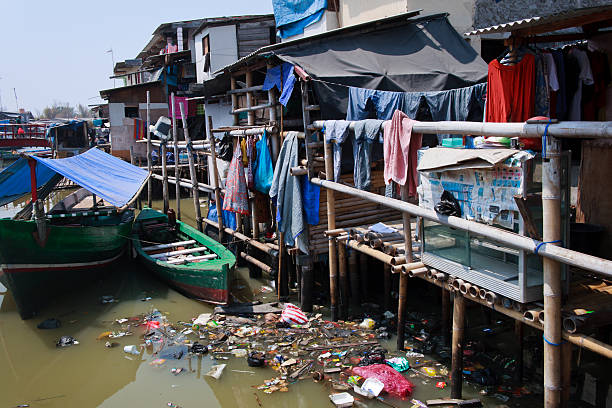 Living on a junkyard Jakarta, Indonesia - September 6, 2011: One of Jakarta's slums located not far from business heart of the City. People living in various bamboo or wooden huts build on river full of garbage jakarta slums stock pictures, royalty-free photos & images