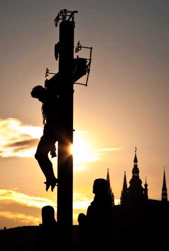 Praha, Czech - June 8, 2010: Statue of Jesus Christ on the cross. The picture was taken in Prague, Czech Republic on the Charles Bridge at sunset. In the background you can see the Cathedral of St. Vitus.