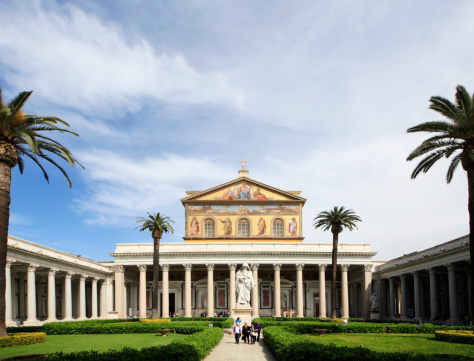 Rome, Italy - May 5, 2013: The Basilica of St Paul (Italian: Basilica di San Paolo fuori le Mura) is one of four churches considered to be the great ancient basilicas of Rome. Tourists visiting the church and walking in the garden of the church.