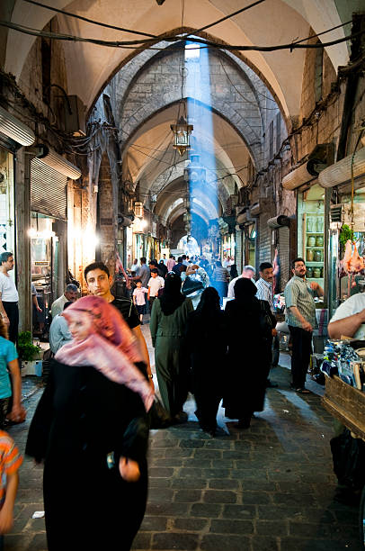 Aleppo, Syria - June 24, 2010: A shaft of light falls through an opening in the roof of the historic souk in Aleppo as shoppers walk down the corridor.