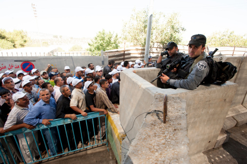 Bethlehem, Occupied Palestinian Territories - August 17, 2012: Israeli soldiers watch as Palestinian men wait at the Bethlehem checkpoint on the final Friday of Ramadan.