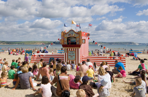 Weymouth, England - August 31, 2012: Holiday makers sitting on the sands of Weymouth beach to watch a traditional Punch and Judy