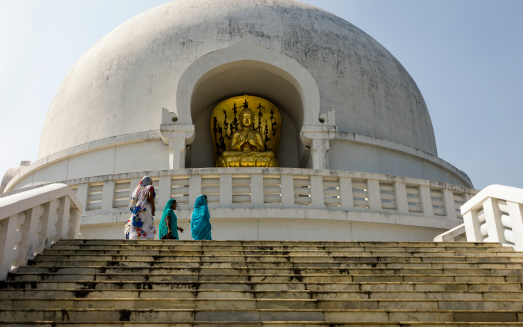 Patna, India - October 14, 2011: a photograph of devotees climbing the stemps to the World Peace Pagoda in Vaishali, Patna, India. The World Peace Pagoda is a shrine to the Buddhist faith. The shot was taken in late Autumn at the end of the monsoon season in India. A gold leaf figure of the Buddha can be seen in the centre of the photograph.