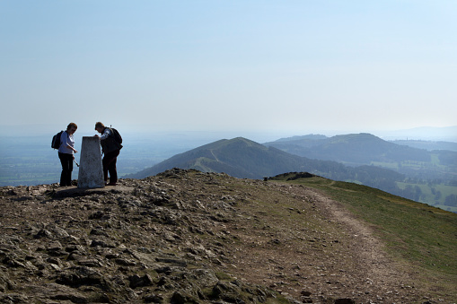 Malvern, UK - 29th March 2012: Two women examine the old trig point on Worcester Beacon on top of the Malvern Hills, Worcestershire, UK. Worcestershire Beacon, also known as Worcester Beacon is a hill whose summit at 425 m (1,395 ft) is the highest point of the range.