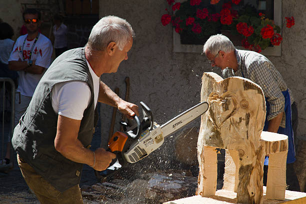 Moena (Dolomites) - Carpenter builds a chair Moena, Trentino, Italy - August 19, 2012: Moena (Dolomites) - A Carpenter builds a chair with a chainsaw during a summer show for tourists (Neighborhood party turkish), on background another carpenter is cleaning the floor and many tourists are watching the show. catinaccio stock pictures, royalty-free photos & images