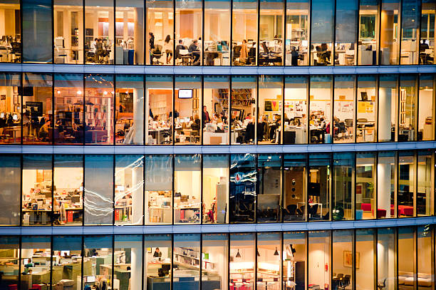 Workers in modern office building London, UK - January 31st, 2013: people working in the More London Riverside Estate building at dusk. Full-time employees in the UK work longer hours than the EU average, according to the Office for National Statistics data. office window night stock pictures, royalty-free photos & images