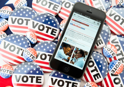 Florence, Italy - September 30, 2012: The new Apple Iphone 5 showing the US election page on the Guardian website. The smartphone is over a group of vote badge button for the 2012 US Election. The iphone 5 is the new smartphone made by Apple Inc. It was released on September 21st 2012, the iPhone 5 is Apple's first mobile phone with a 4