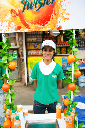 Delhi, India - February 26, 2008: Hostess trying to promote artificial fruit juices in front of a traditional fresh fruit stall on February 26, 2008 in Delhi, India. This is where traditional meets modernity