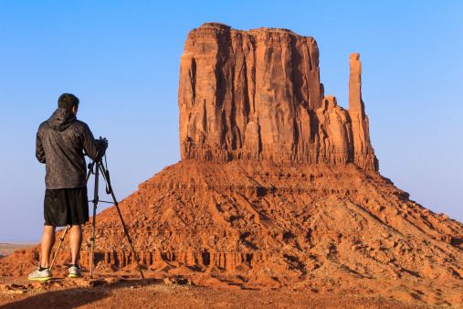 Monument Valley, USA - April 15, 2011: Male Photographer taking picture with camera on tripod of mesa at Monument Valley