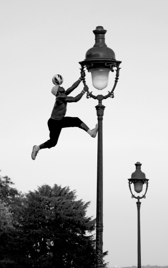 Paris, France - August 30, 2013: Freestyle footballer Iya Traore from Guinea plays football climbing up a lamppost on the hill of Montmatre. Hanging on the cast-iron historic lamp he balances a football on his head. Almost every day in summer Iay Traore demonstrates his skills in front of many tourists.