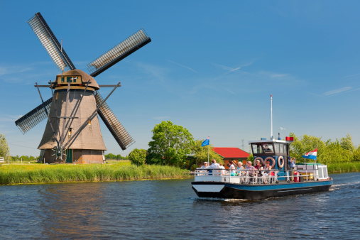 Kinderdijk, Netherlands - May 26, 2012: Sightseeing boat with tourists on the river in Kinderdijk near a windmil. The windmills of Kinderdijk became a UNESCO World Heritage Site since 1997.