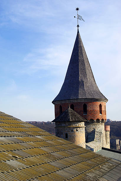 Kamianets-Podilskyi, Ukraine-May 15, 2021:Old wooden conical roof of the stone tower. Roof of the ancient tower against blue sky.