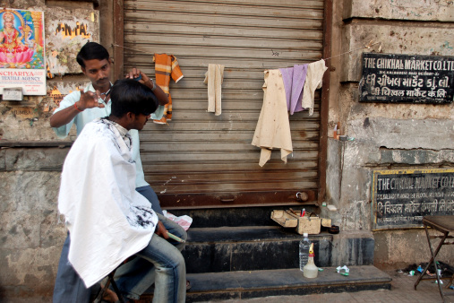 Mumbai, India - November 19, 2006: street hairdresser cutting hair to the man in the improvized \