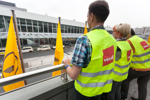 Frankfurt, Germany - April 22, 2013: Ground staff of Lufthansa entered into a one-day token strike. Members of german trade union verdi with yellow reflective vests are looking at Terminal 1, Airport Frankfurt, in the background some flags of Lufthansa.