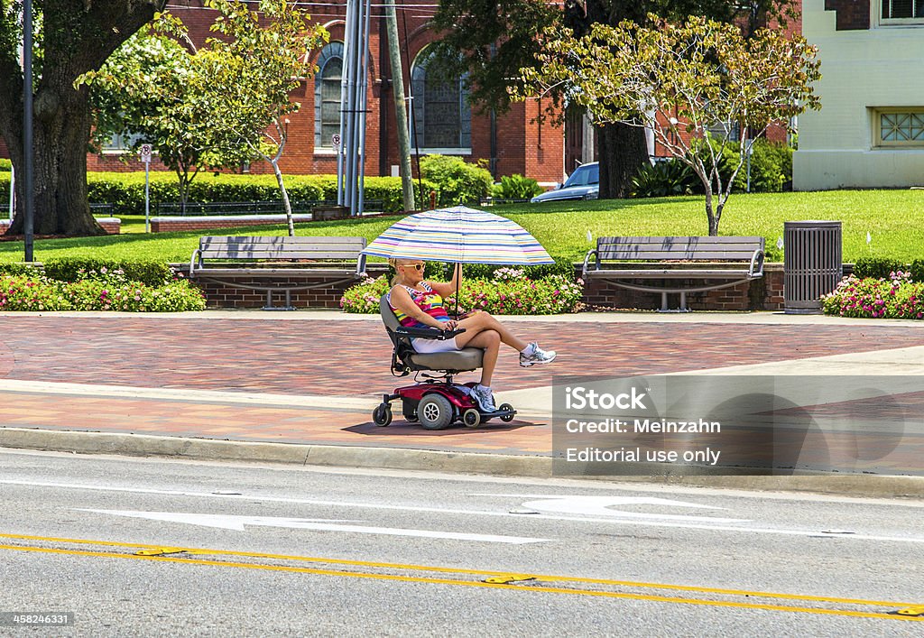 attracive lady rides in her electric wheelchair with a parasol Lake Charles, USA - July 12, 2013: attracive lady rides in her electric wheelchair  in Lake Charles, USA. Electric wheelchair was invented after WW2 by George Johann Klein for the injured war veterans. Heat - Temperature Stock Photo