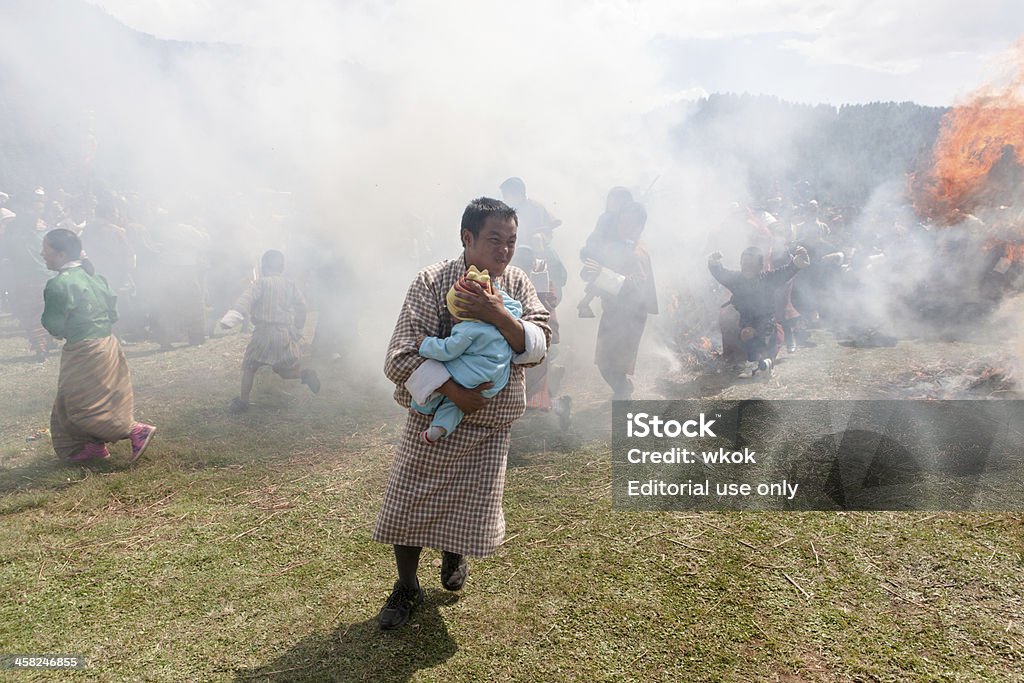 Buthanese uomo che tiene il bambino passa attraverso due bruciare haystacks - Foto stock royalty-free di Bhutan