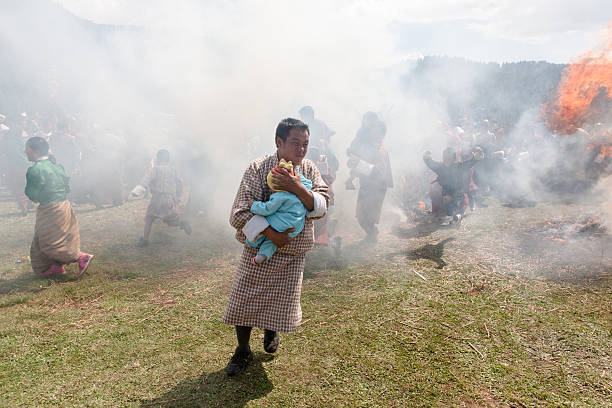 Buthanese uomo che tiene il bambino passa attraverso due bruciare haystacks - foto stock