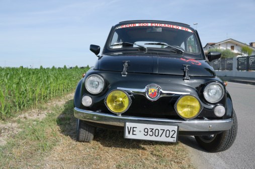 Saonara, Italy - May 29, 2011: Vintage tuned small Fiat 500 car parked near a corn field. The scorpion logo is the symbol of Abarth, an Italian racing car maker, famous for Fiat car tuning. The original Fiat 500 is a car produced by Italian automaker Fiat. It was built from 1955 to 1975 and is generally considered an icon of Italian economic boom. Shot along a public street.