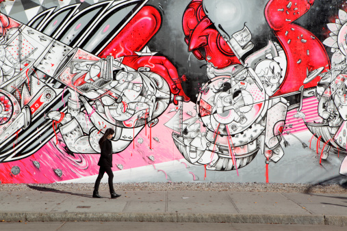 New York, NY, USA: December 6, 2012: A young New Yorker walks to work into the sunrise along Houston Street on the Lower East Side of Manhattan past the Bowery Mural Wall. The mural wall features a changing array of street art works. The one on display here is \