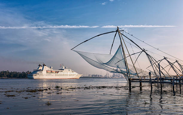 Passenger ship & Chinese fishing nets, Cochin, Kerala, India. Fort Kochi, India - January 06, 2012: a passenger ship enters Cochin harbour lined with traditional Chinese fishing nets on a calm winter evening. This photo depicts the juxtaposition between the old and the new. cochin kerala india chinese fishing net stock pictures, royalty-free photos & images