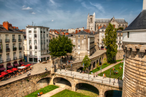 Nantes, France - August 20, 2011: The main entrance of Castle of Brittany Duke's. Many tourists and some banners on the bridge. many people sitting on tables of restaurant  and St. Peter Cathedral on background