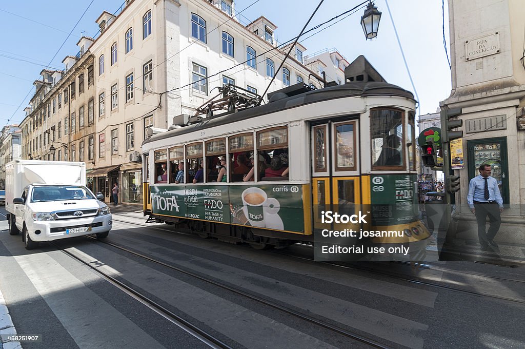 Lisbon Yellow Tram Lisboa, Portugal _ September 11, 2012: The Lisbon tram network is run by Carris, the municipal transport company in Lisbon. Currently consists of five lines. Has 165 drivers and a fleet of 58 vehicles, 40 historical, 8 light and 10 articulated, with a single base station in Santo Amaro. Historical lines, with their bright yellow or red trams are used by many tourists.A tram with several passengers on board, traveling on the Rua da Conceicao, next to a pickup truck.A pedestrian waiting time to cross the street. Adult Stock Photo