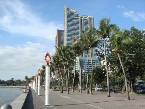 Manila, Philippines - January 17, 2009: scenic baywalk on Manila bay, Roxas boulevard. In the background a group of Filipinos swimming on the bay.