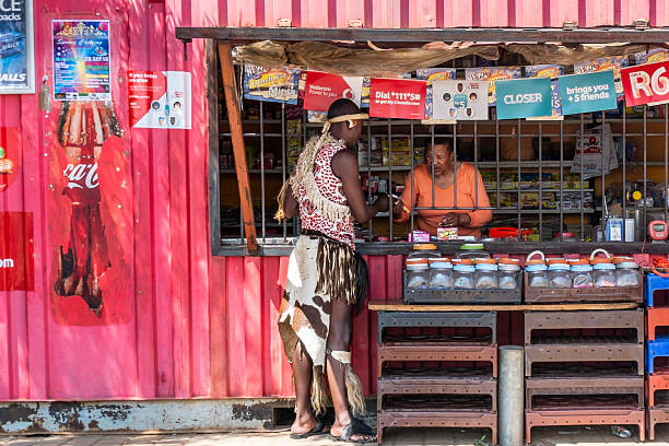 African man shopping at the spaza Johannesburg, South Africa - September, 24th 2013: African zulu man dressed in his traditional clothing, shopping at a spaza shop in Orlando, Soweto. Shop is made from an old shipping container with signs and posters seen stuck on. Burglar proofing for safety. soweto stock pictures, royalty-free photos & images