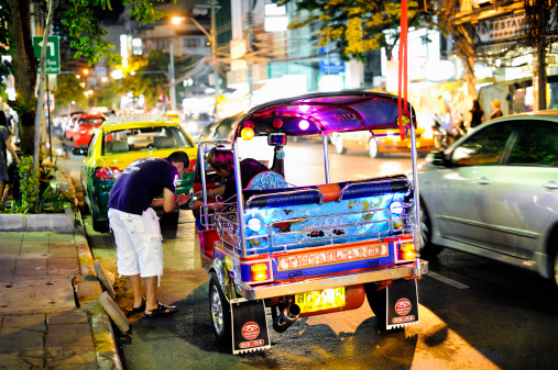 Bangkok, Thailand - July 9, 2010: Street scene in the Bangkok city center at night. A tuk-tuk driver and a customer are comparing data on their cell phones. Tuk-tuks are a common means of public transportation in Thailand.
