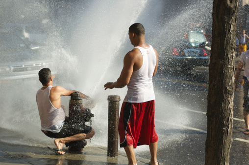 New York City, USA - July 16, 2006: Two young men open a fire hydrant in Washington Heights in upper Manhattan. The fact that tampering with fire hydrants is illegal does not stop people from opening them on hot summer days.