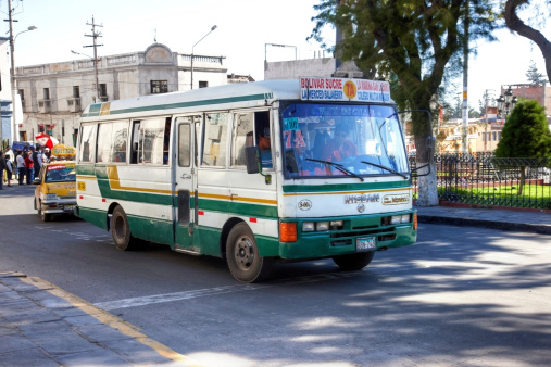 Arequipa, Peru - May 25, 2013: Typical Peruvian public transport bus in service on the cobblestone streets of Arequipa. A yellow taxi and pedestrians are also pictured
