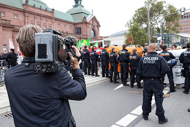 Protests against NPD election campaign Wiesbaden, Germany - August 26, 2013: Counterprotestors against a NPD election campaign speech in the city center of Wiesbaden. In the foreground a riot police cordon trying to separate Nazis and protestors from each other. Founded in 1964 the NPD is a German nationalist party, its agitation is racist, antisemitic and revisionist. A camera operator of German TV is filming the scenery. national democratic party of germany stock pictures, royalty-free photos & images