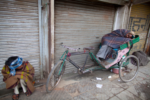 New Delhi, India - February 23, 2013.  Two Indian pedicab drivers, one awake and one sleeping, will shortly begin their 18 hour work day in the old part of the city.
