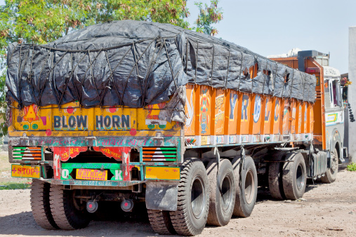 Gujarat, India - Fruary 28, 2013: Colorful Indian heavy goods vehicle parked up at  Dhabha (Indian truck stop) in the mid day sun while the driver and crew take an after noon nap from the heat of the Indian sun.