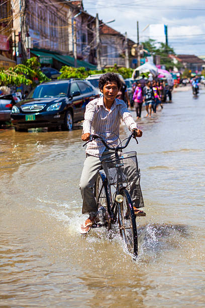 giovani cicli attraverso floodwaters a siem reap, cambogia - floodwaters foto e immagini stock